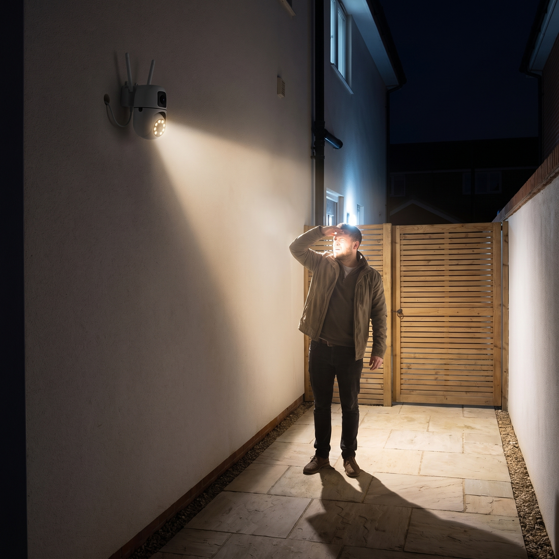 A man at a side gate at night lit by the camera's own spotlights