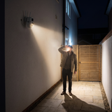 A man at a side gate at night lit by the camera's own spotlights